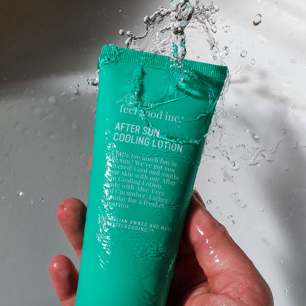 Hand holding a green tube of after sun cooling lotion with water splashes in the background