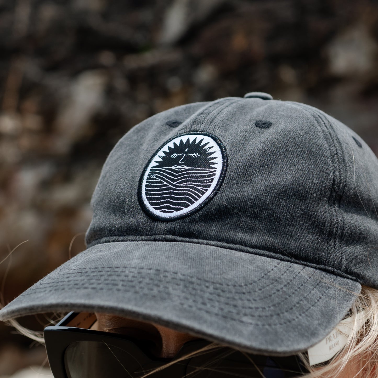 Woman wearing Selkia naturally dyed black faded coloured peak cap with sun and ocean embroidery design