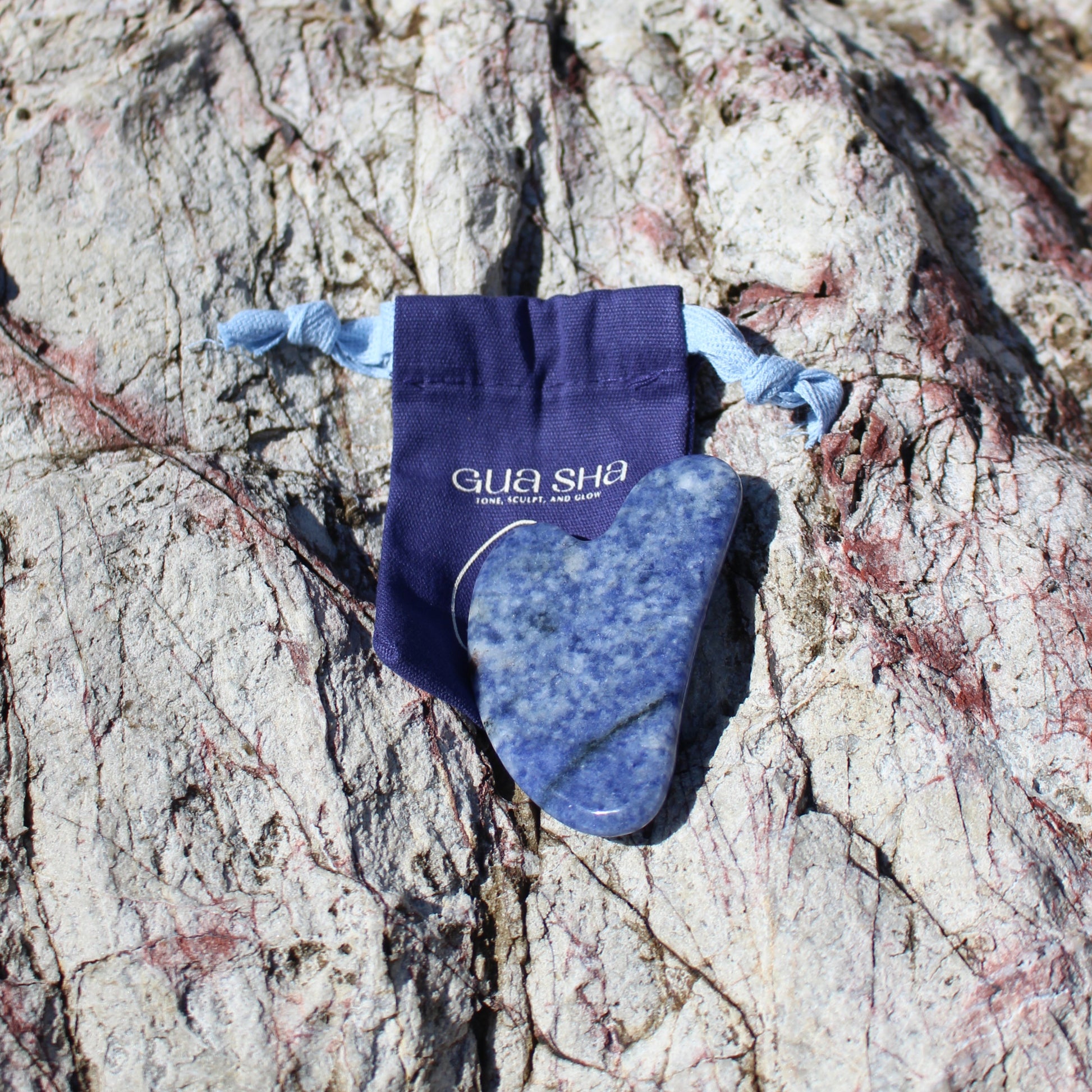 Selkia Gua sha blue stone face massage tool with carrier bag on stone background