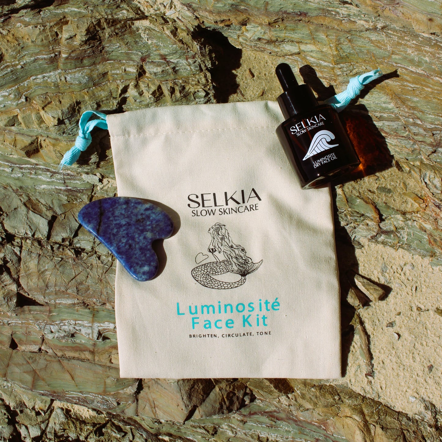 Australian made Selkia natural face dry oil serum and Gua sha face massage tool with drawstring canvas carrier bag on beach stone background