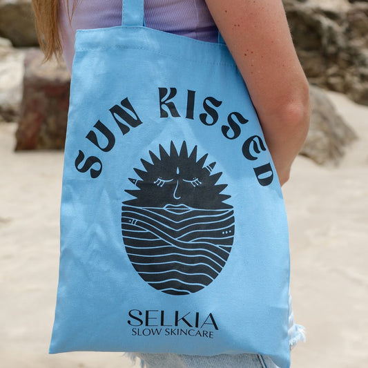 Close up of woman wearing a Selkia sunkissed blue tote bag with beach background