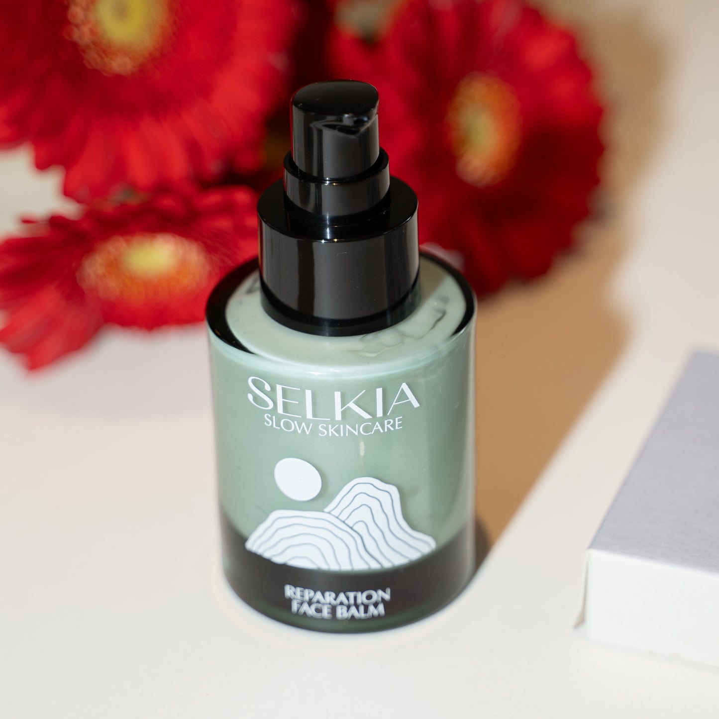 Selkia skincare balm bottle with red flowers in the background